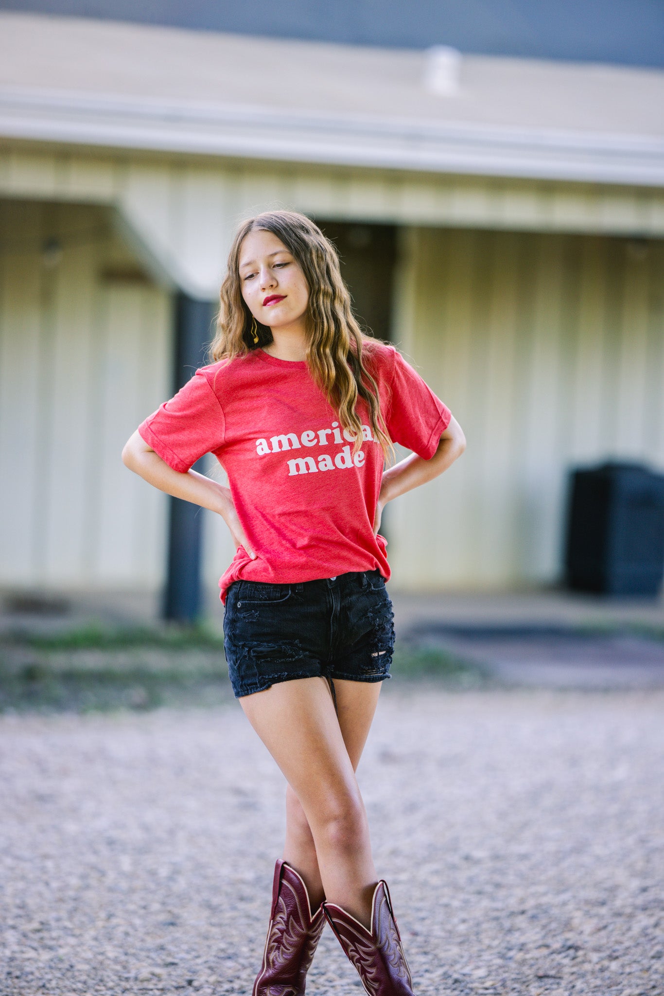 T-shirt with the text "American Made," celebrating patriotism and pride in American craftsmanship and style. Red Shirt and girl wearing cowboy boots.
