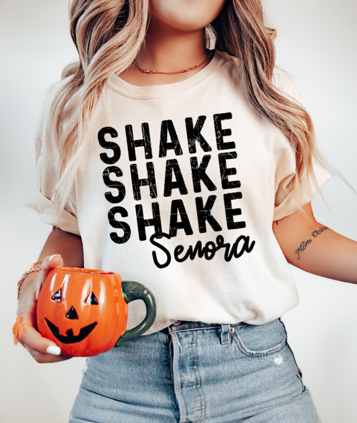 Person wearing a white t-shirt with 'SHAKE SHAKE SHAKE Senora' text, holding an orange pumpkin mug.