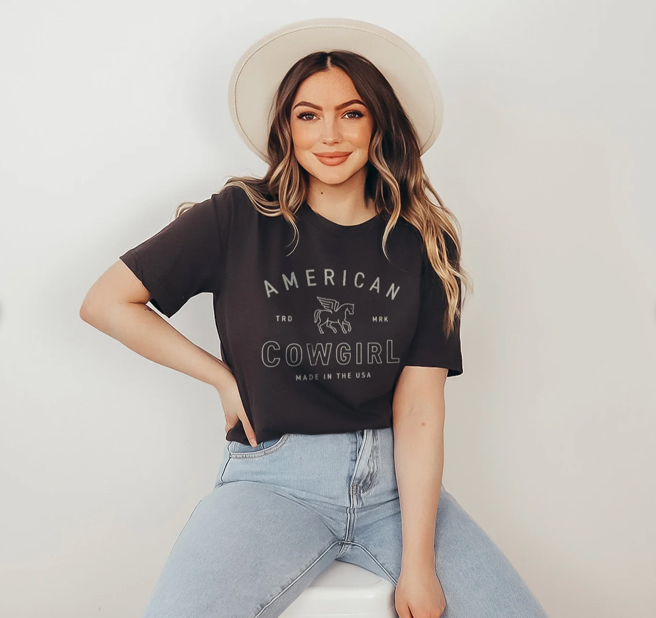 Black t-shirt with the text "American Cowgirl" in a western-style design, perfect for showcasing country pride and rodeo style. Girl wearing cowboy hat and graphic tee.